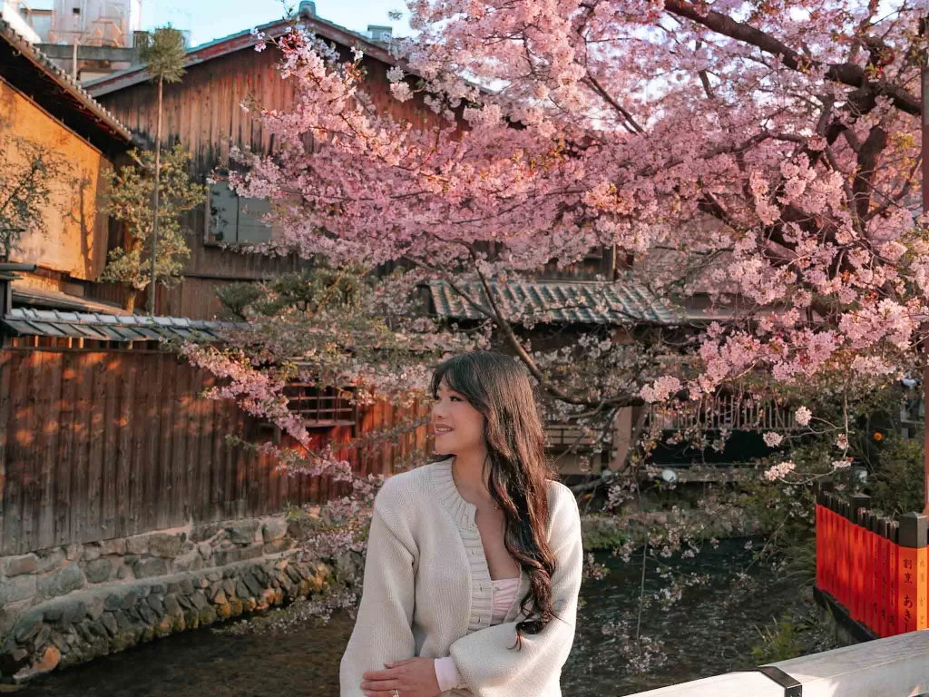 Angelia sitting on a bridge surrounded by cherry blossoms at gion street in Kyoto