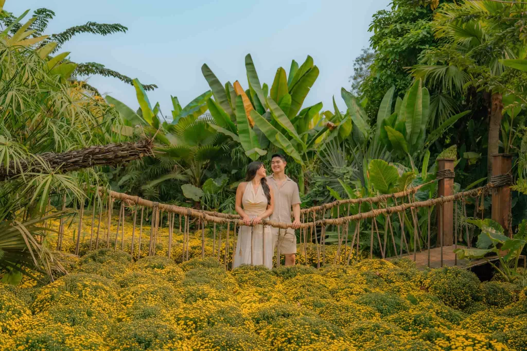 Angelia and Chris standing on a bridge in front of a flower field at Cai To Chim